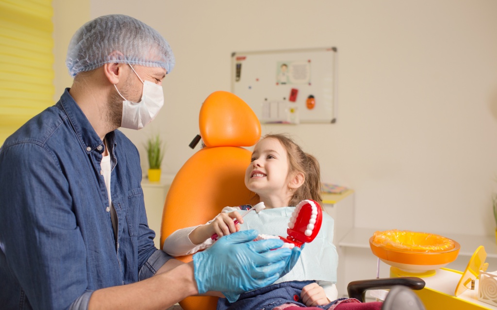 a male dentist teaches a little girl how to brush her teeth properly with a toothbrush.